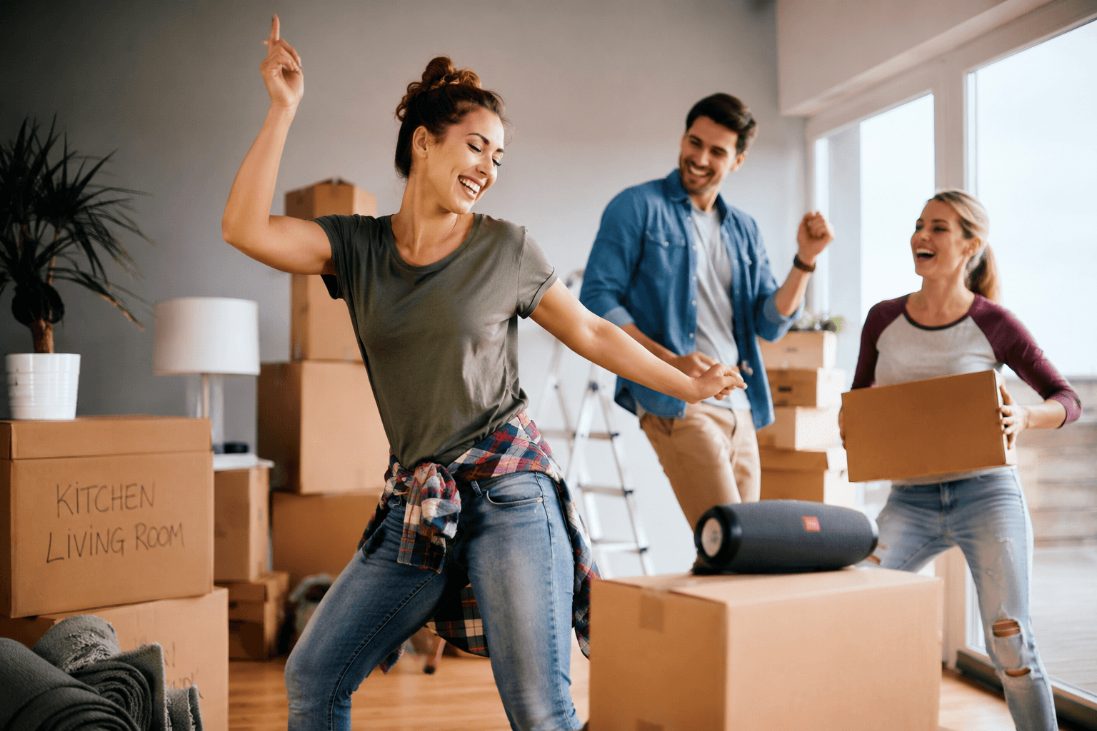 Friends dancing and laughing while packing moving boxes, making moving day more enjoyable and less stressful.