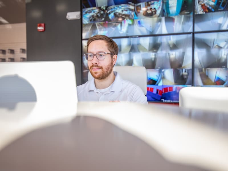 Modern Storage® employee at a desk reading a storage unit rental agreement with security camera feeds displayed in the background