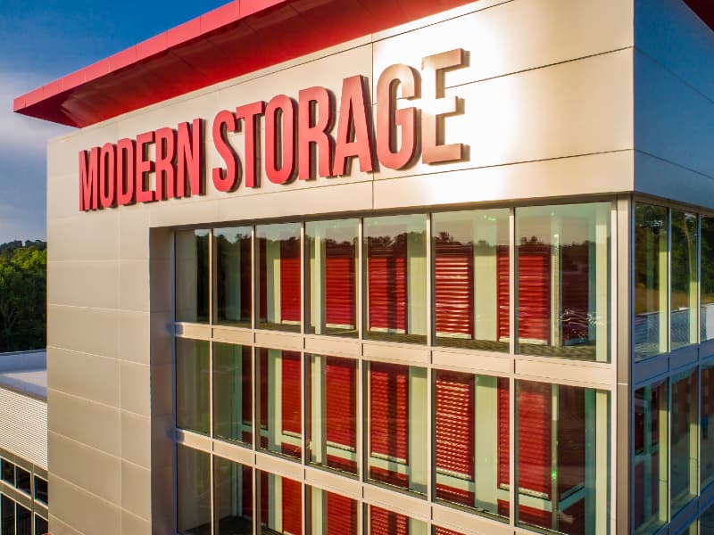 Exterior view of a Modern Storage® multi-story facility in Arkansas with red roll-up units visible through glass walls, offering secure and climate-controlled storage.