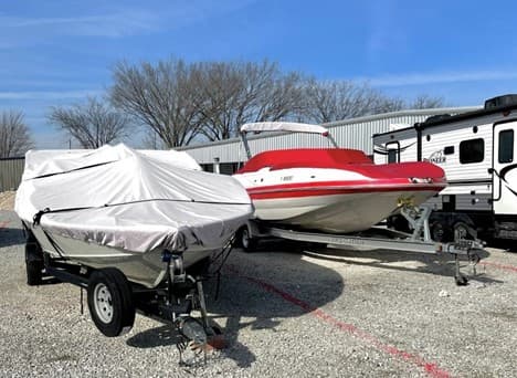 Two boats and an RV parked in gravel lot at Modern Storage® outdoor vehicle storage facility