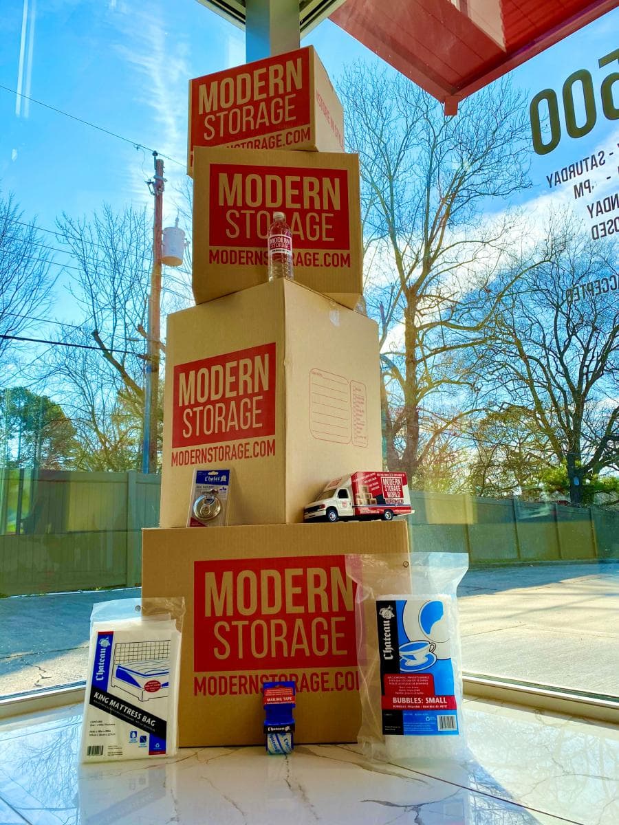Stack of Modern Storage® branded moving boxes and packing supplies on display in a sunny window corner