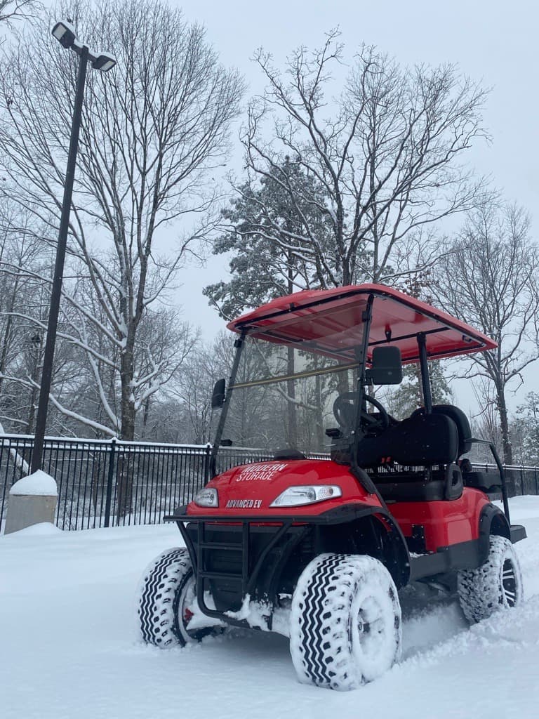 Red golf cart parked outside and covered in snow, demonstrating the risks of improper seasonal storage for vehicles like golf carts and ATVs during winter.