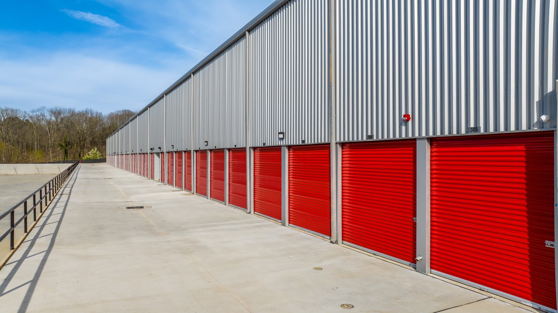 Modern Storage® facility exterior with a long row of red roll-up drive-up storage unit doors under a metal building
