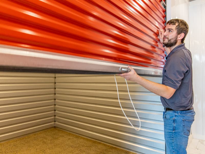 Modern Storage® employee lifting a red roll-up door to show the interior size of a standard storage unit for square footage reference
