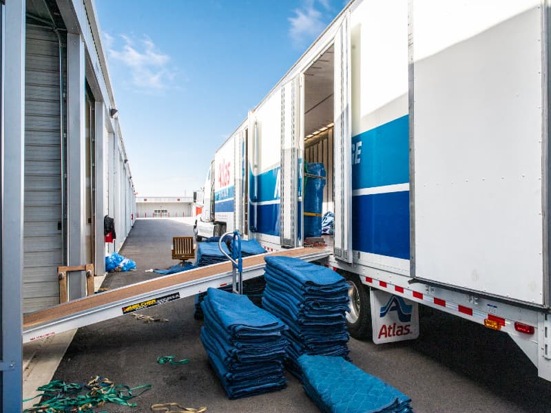 Moving trucks unloading business items at Modern Storage® facility in Arkansas with moving pads stacked nearby