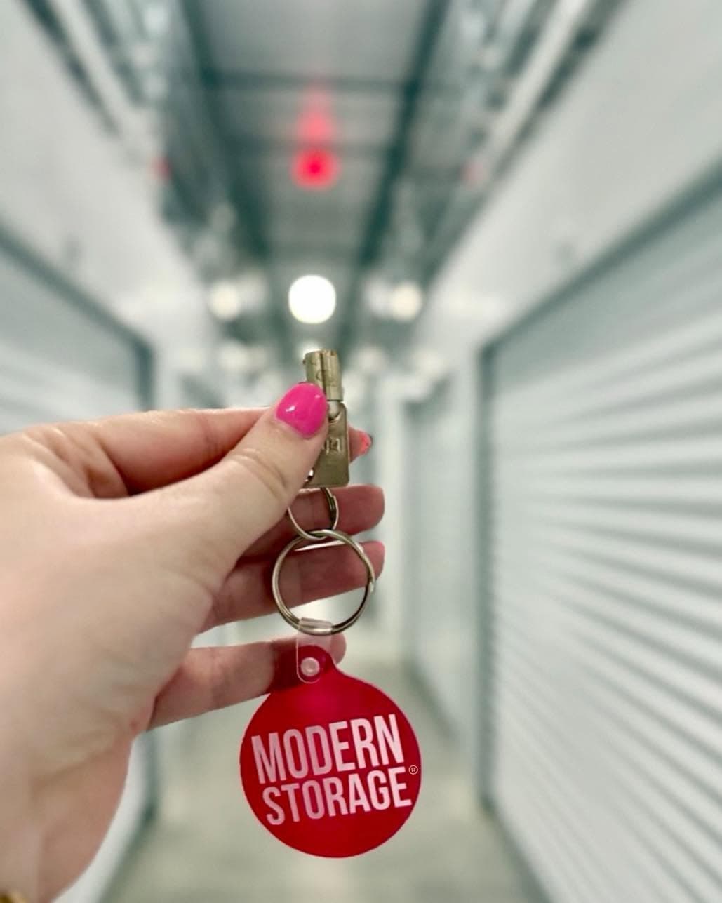Hand holding a Modern Storage unit key in a clean climate-controlled storage hallway.