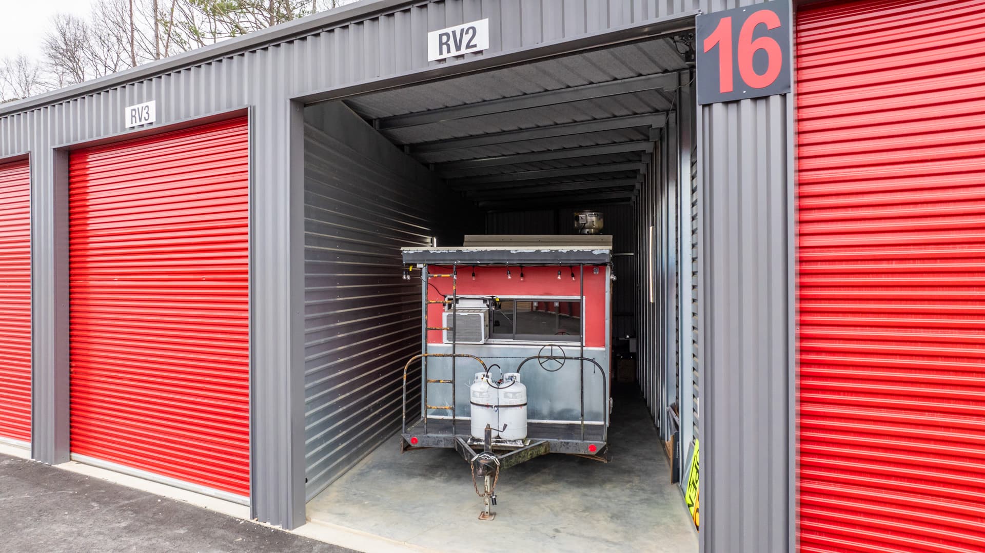 Modern Storage® Shackleford drive-up storage units with wide paved driveways, red roll-up doors, and gated secure access in L