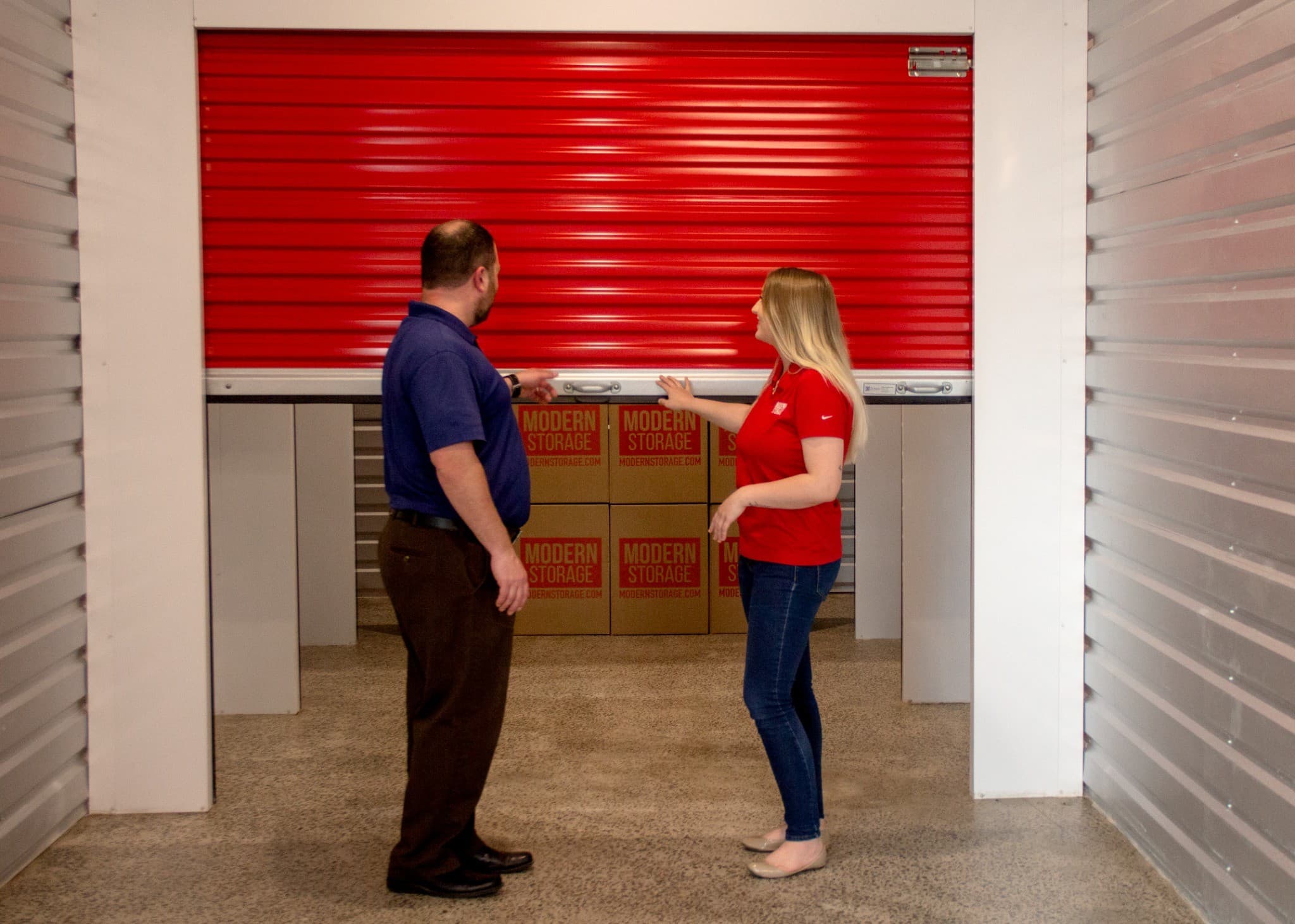 Modern Storage team helping a customer access a clean storage unit with organized moving boxes inside.